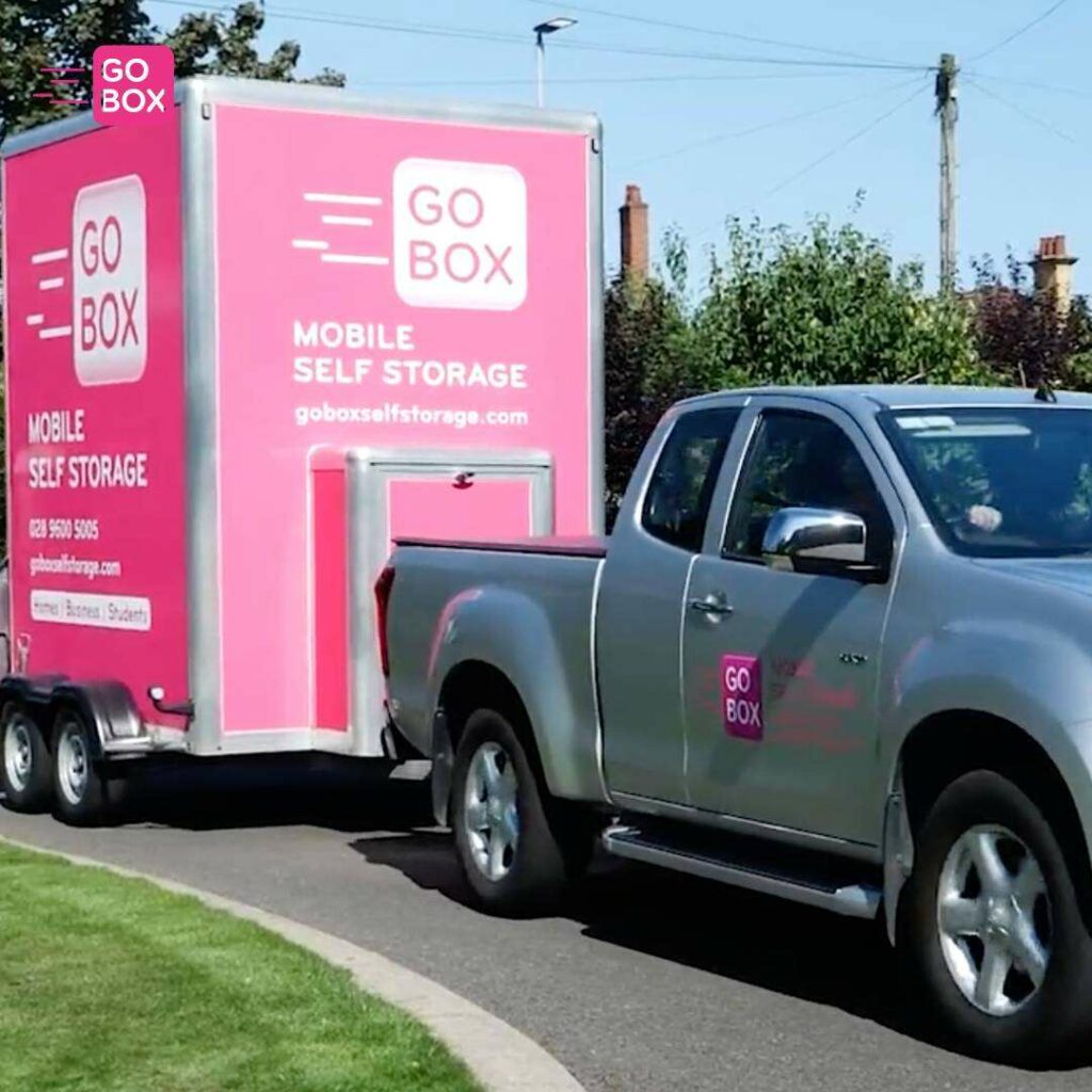 A silver pickup truck towing a pink mobile self-storage unit from go box.