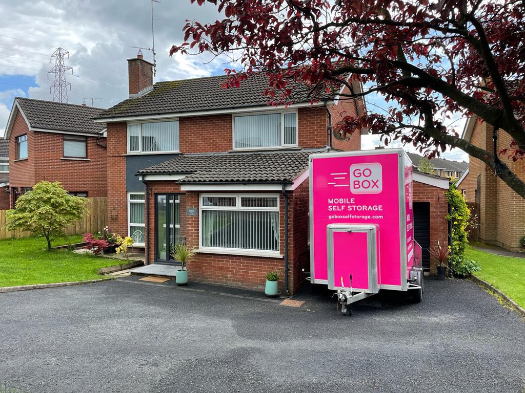 A bright pink mobile self-storage unit parked in the driveway of a residential home offers convenient ways to help with your storage needs.