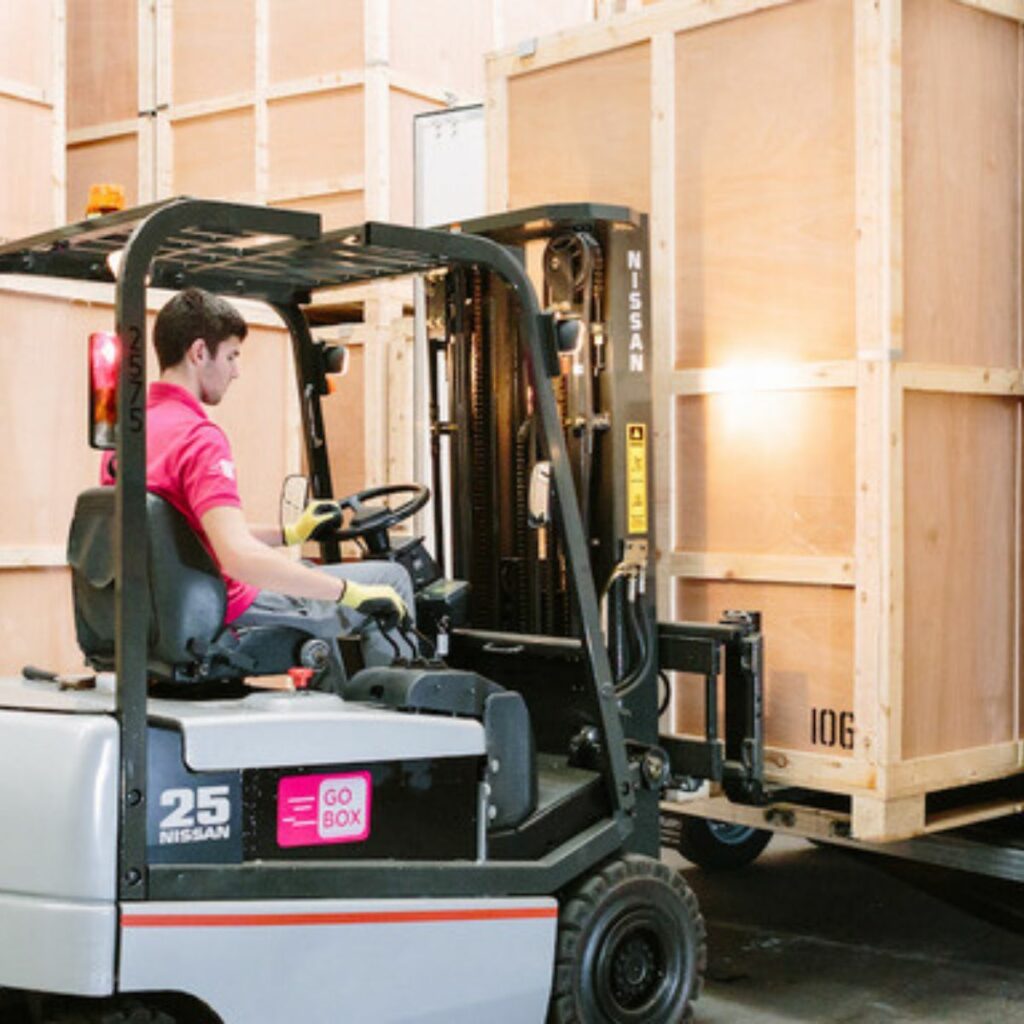 Man operating a forklift near wooden crates in a warehouse.