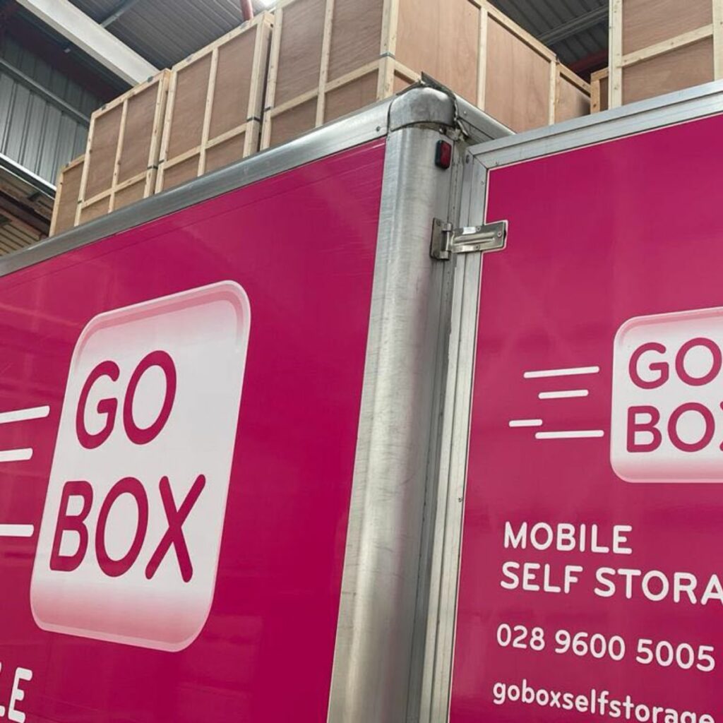 A pink go box mobile self-storage unit, perfect for any Business Owner Belfast, with contact information displayed on the side.