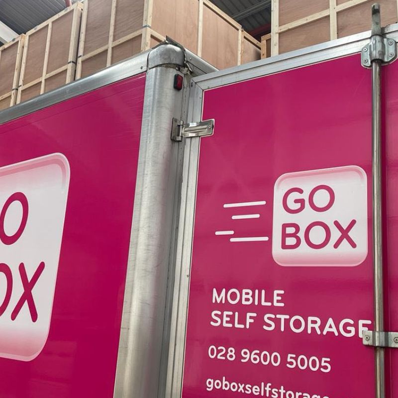 A close-up of a magenta-colored go box mobile self-storage unit with contact information visible.