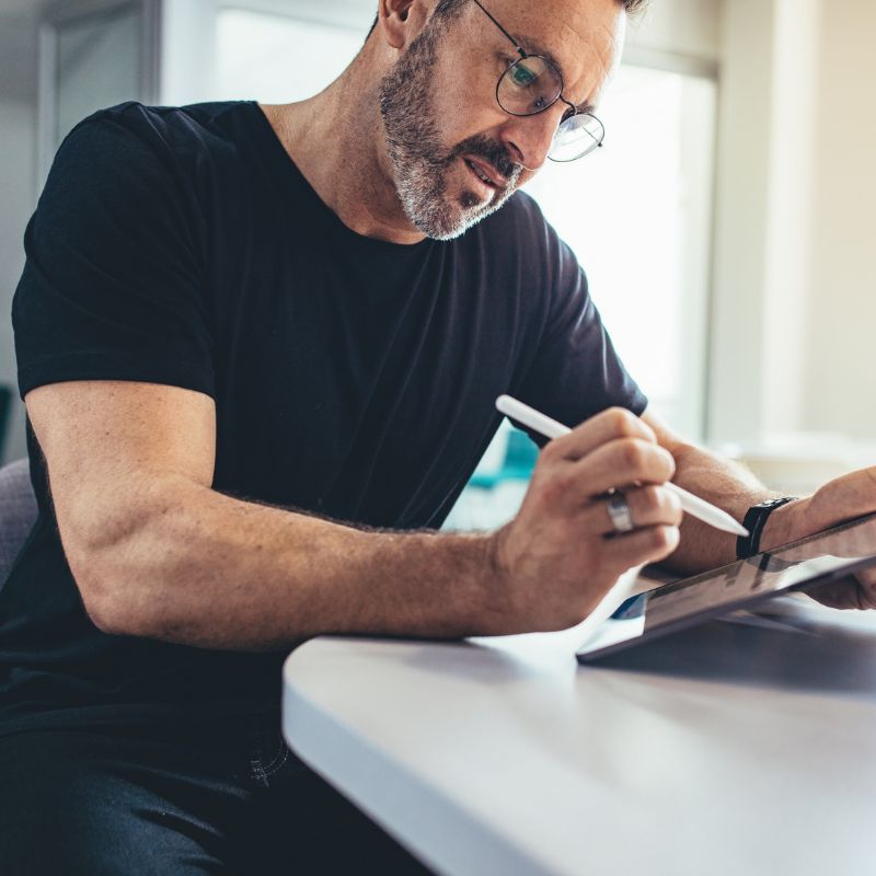 A man with glasses focusing on writing in a notebook while seated indoors.