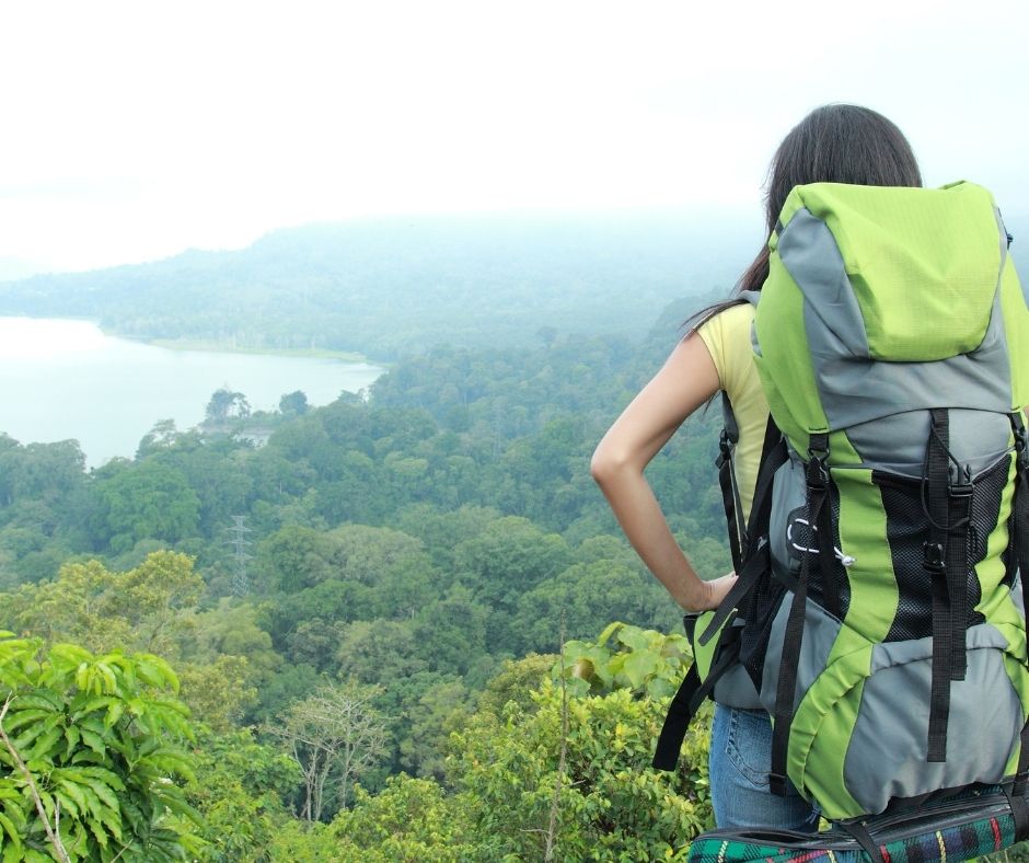Female hiker with a backpack overlooking a misty forest landscape and a lake.