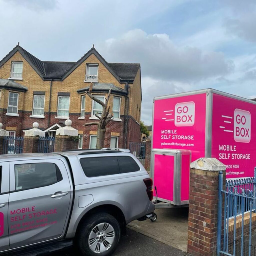 A storage company vehicle and a mobile self-storage unit, offering advantages of using self-storage, parked near a residential building under a cloudy sky as residents prepare to move.