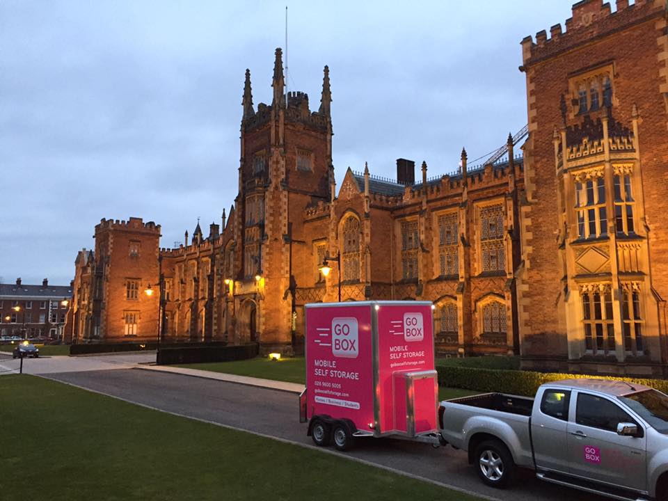 A mobile storage unit parked in front of a historic gothic-style building at dusk.