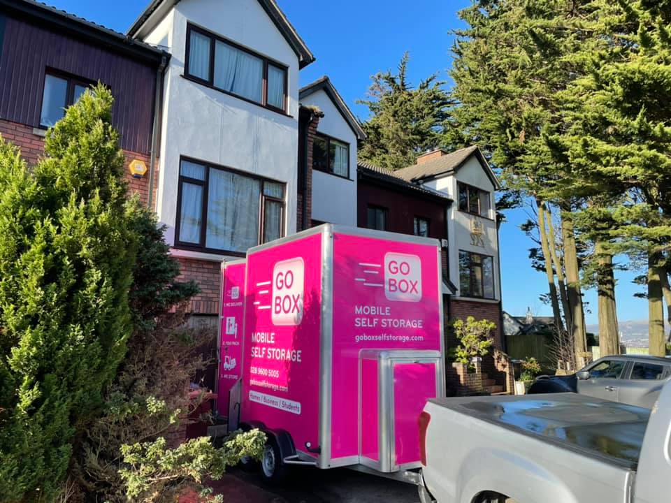 A bright pink gobox mobile self-storage trailer parked next to a suburban house on a sunny day.