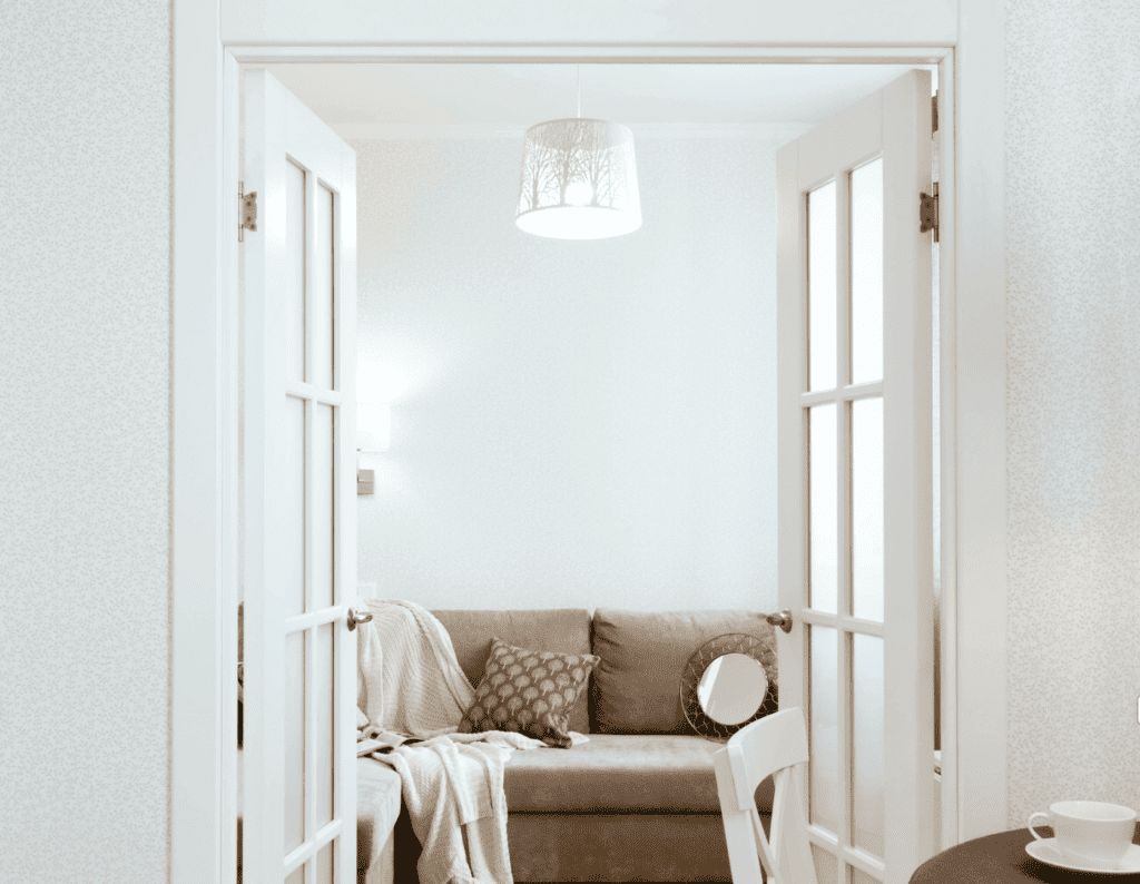 A cozy nook with a comfortable couch and a hanging lamp, viewed through an open double door.