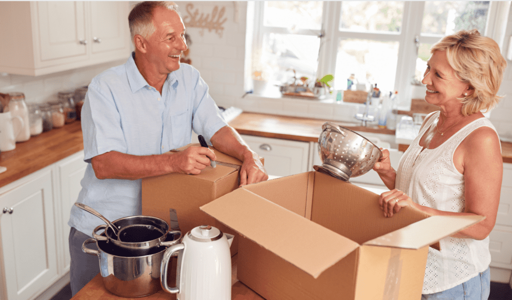 A mature couple unpacking kitchen items from cardboard boxes and smiling at each other.