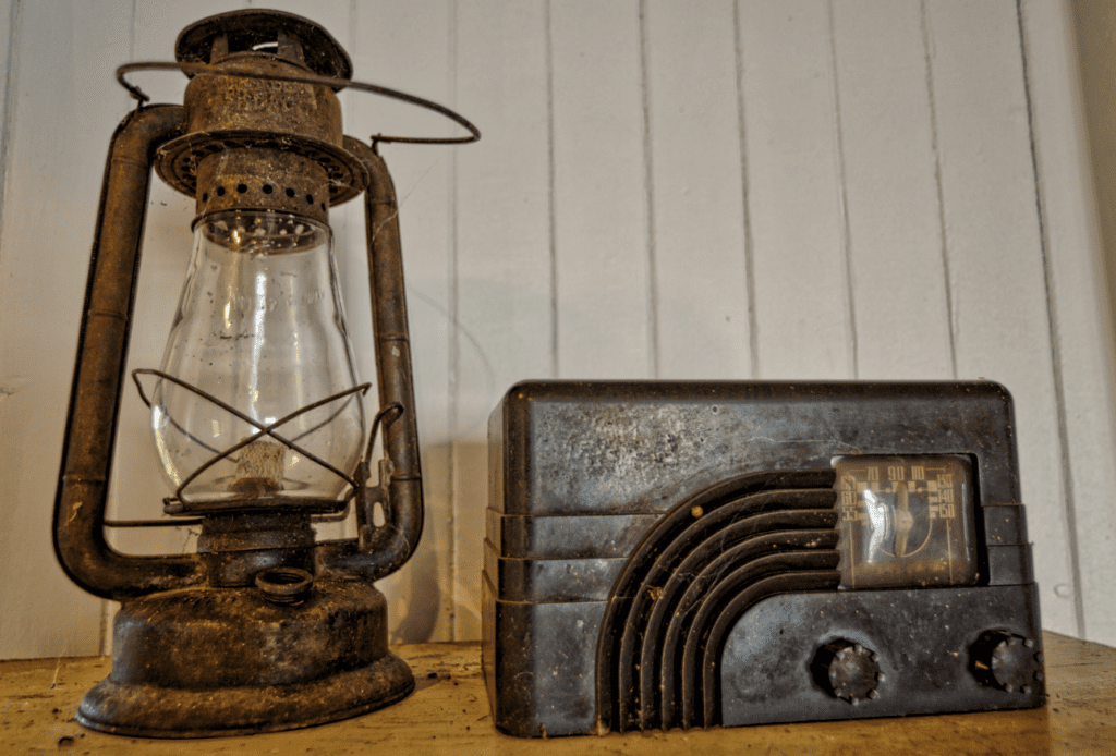 Vintage oil lantern and old-fashioned radio on a wooden surface with a white wall in the background.