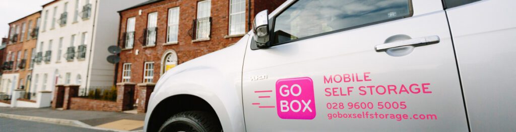 A mobile self storage company van parked on a street with buildings in the background.