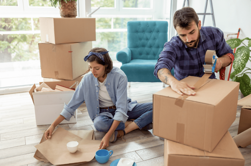 A man and a woman learning how to pack items into cardboard boxes in a room suggestive of moving house.