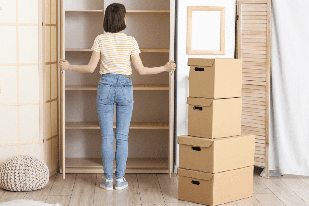Woman standing in front of empty wardrobe with cardboard boxes stacked beside her