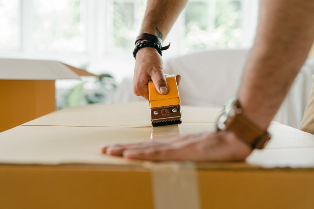 A living room in the process of packing, with labeled boxes and packing tape on a box.