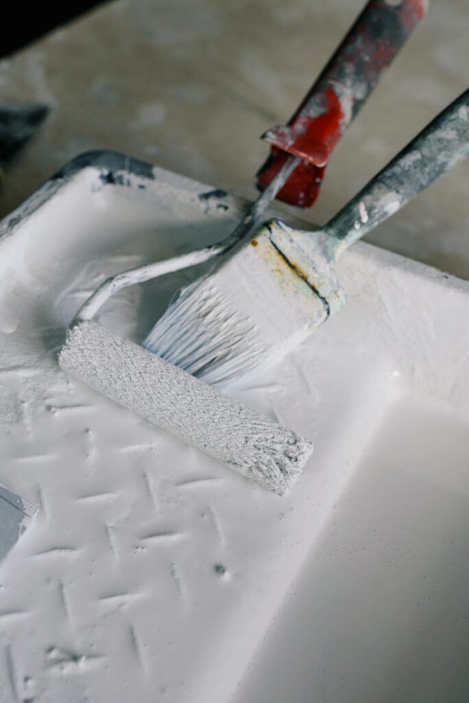 Painting supplies with a roller and brush dipped in white paint.