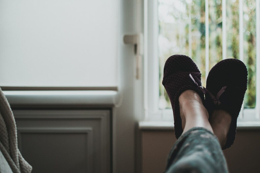 Person relaxing with feet up wearing slippers near a window.