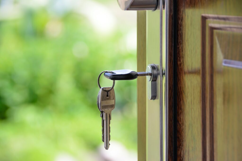 Keys inserted into a door lock with blurred green background.