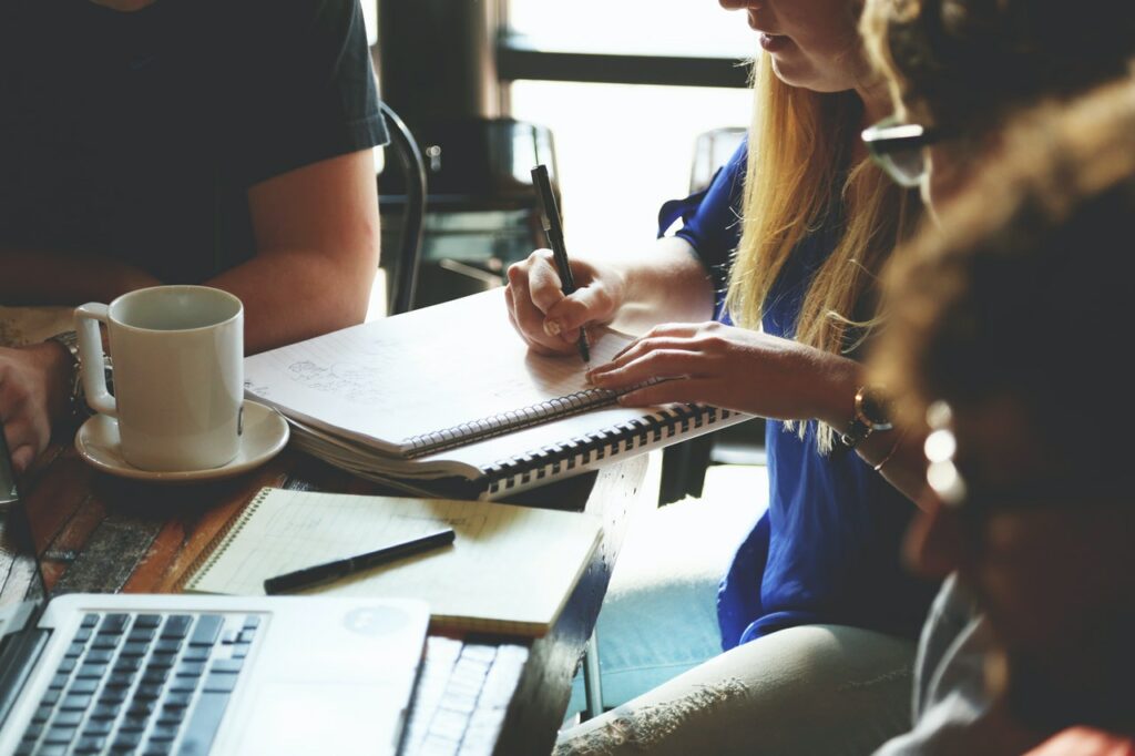 Group of people engaged in a meeting with notebooks and a laptop on a wooden table.