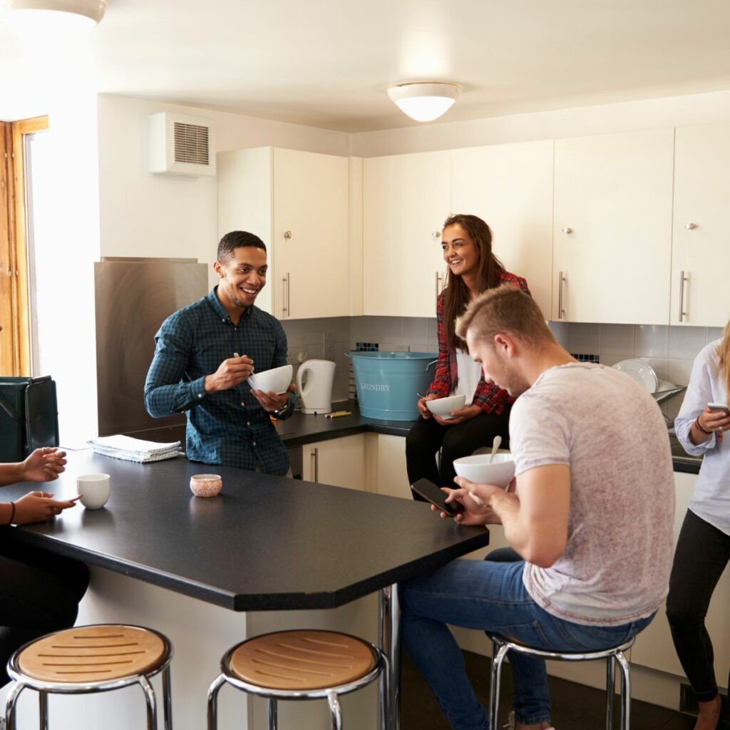 Group of friends enjoying a casual conversation in the kitchen while planning their moving between student accommodations.