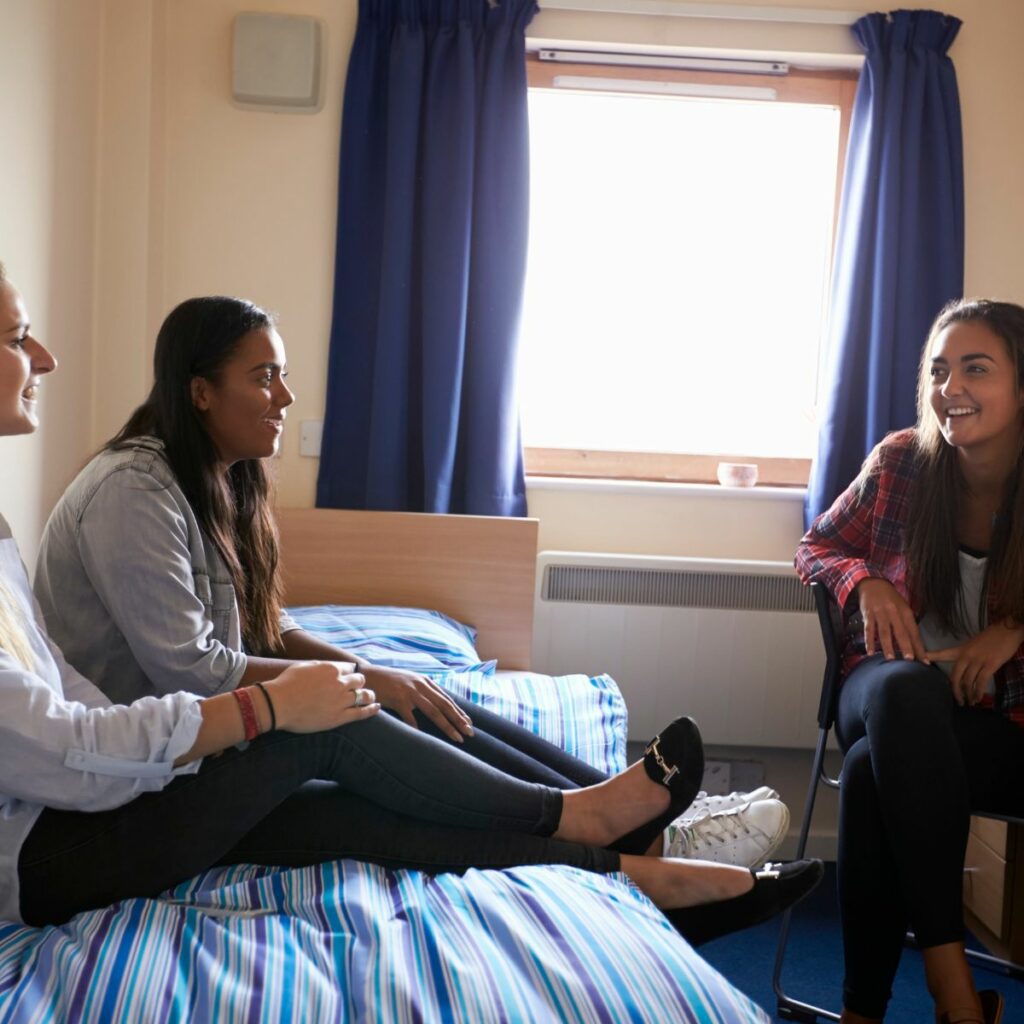Three friends chatting and laughing in their student accommodation in Belfast.