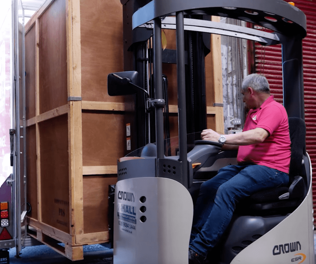 A man operating a forklift to move a large wooden crate in a warehouse.
